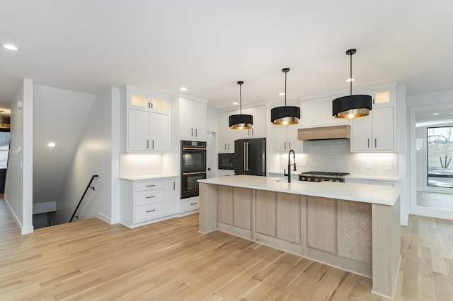 kitchen featuring white cabinetry, backsplash, black appliances, a center island with sink, and decorative light fixtures