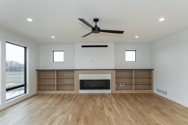 unfurnished living room with ceiling fan, a fireplace, light hardwood / wood-style flooring, and a wealth of natural light