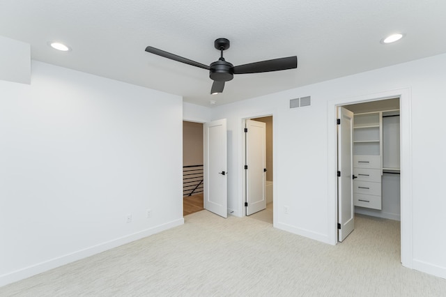 unfurnished bedroom with connected bathroom, a walk in closet, ceiling fan, light carpet, and a closet