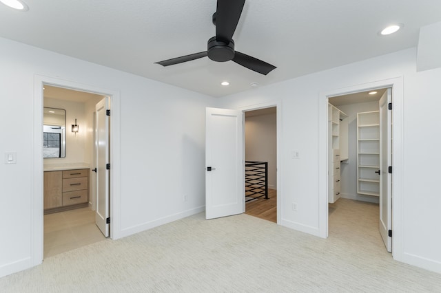 unfurnished bedroom featuring ensuite bathroom, a walk in closet, ceiling fan, light carpet, and a closet