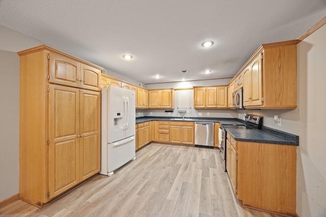 kitchen featuring appliances with stainless steel finishes, a textured ceiling, sink, and light hardwood / wood-style floors