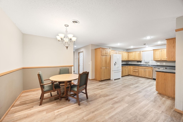 dining area with a notable chandelier, light wood-type flooring, sink, and a textured ceiling