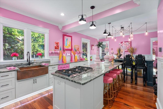 kitchen with stainless steel gas stovetop, white cabinets, wood-type flooring, sink, and a center island