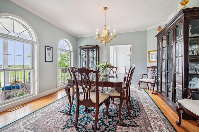 dining room featuring a chandelier, light wood-type flooring, visible vents, and ornamental molding