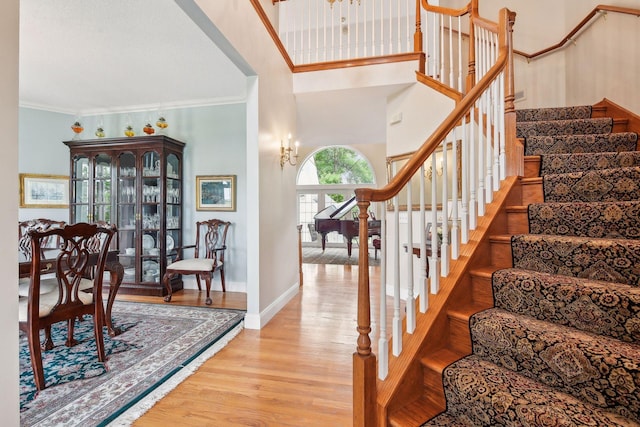 staircase featuring a towering ceiling, crown molding, baseboards, and wood finished floors