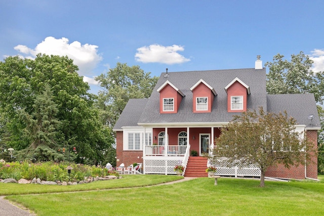 new england style home featuring a porch, roof with shingles, brick siding, and a front lawn