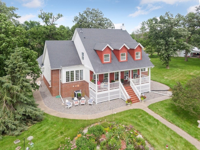 view of front of home with brick siding, a shingled roof, covered porch, a patio area, and a front lawn