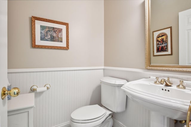 bathroom with toilet, a sink, and wainscoting