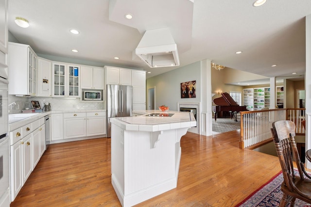 kitchen featuring tile countertops, a fireplace, appliances with stainless steel finishes, a center island, and tasteful backsplash