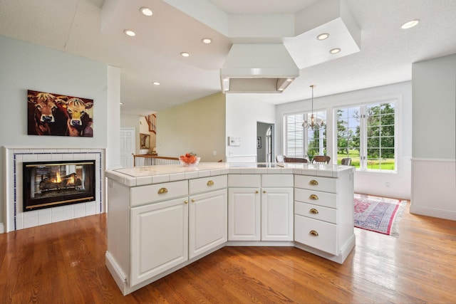 kitchen with tile countertops, light wood-type flooring, a tile fireplace, and white cabinets