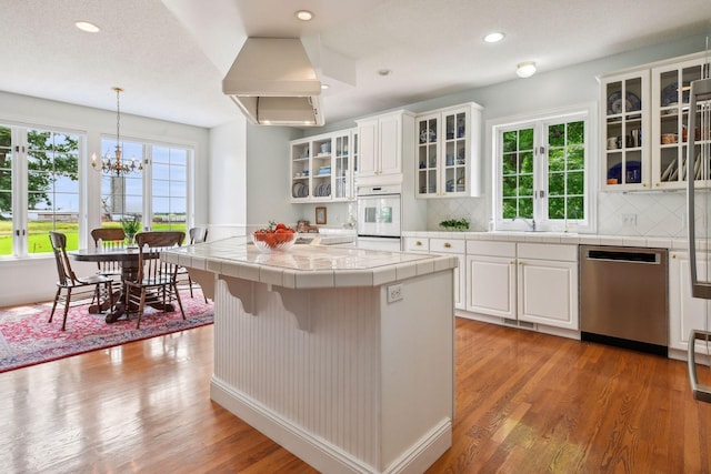 kitchen featuring white oven, tile countertops, tasteful backsplash, light wood-style flooring, and stainless steel dishwasher