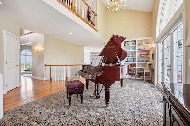 living area featuring baseboards, a towering ceiling, an inviting chandelier, and wood finished floors