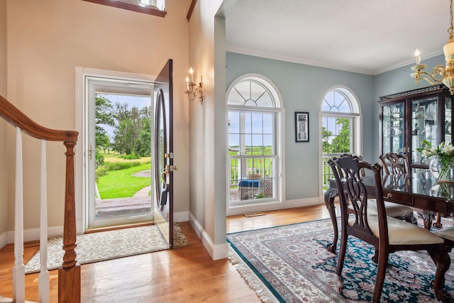 foyer entrance with baseboards, crown molding, light wood-style flooring, and a notable chandelier