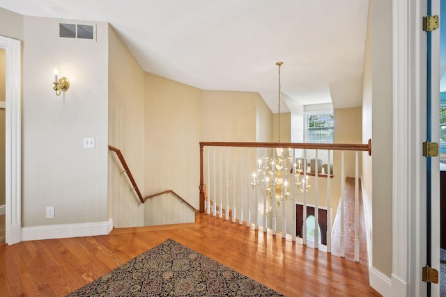 hall featuring a notable chandelier, visible vents, an upstairs landing, wood finished floors, and baseboards