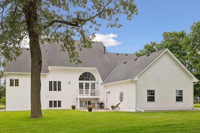 back of property with a yard, roof with shingles, and a patio area