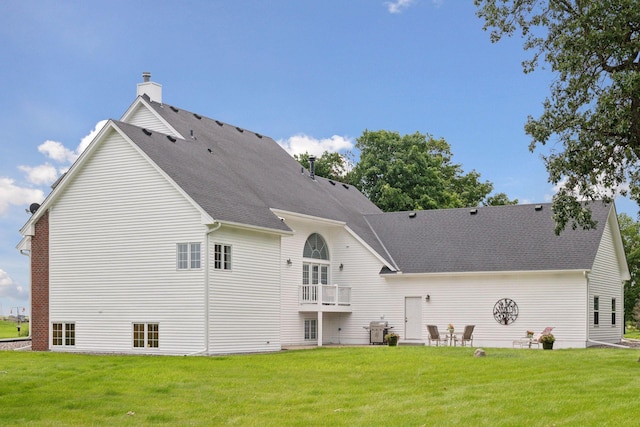 rear view of house featuring a balcony, a shingled roof, a chimney, and a yard