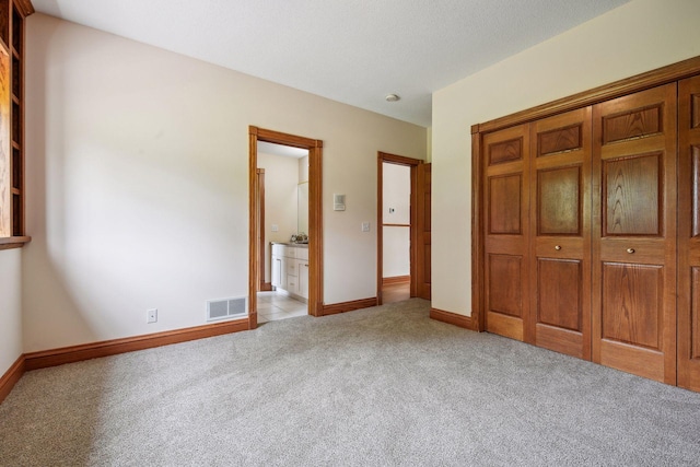 unfurnished bedroom with a closet, visible vents, ensuite bathroom, light carpet, and baseboards