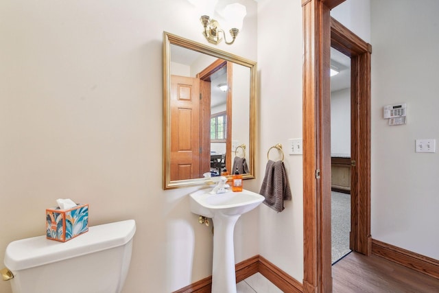 half bathroom with wood finished floors, toilet, and baseboards