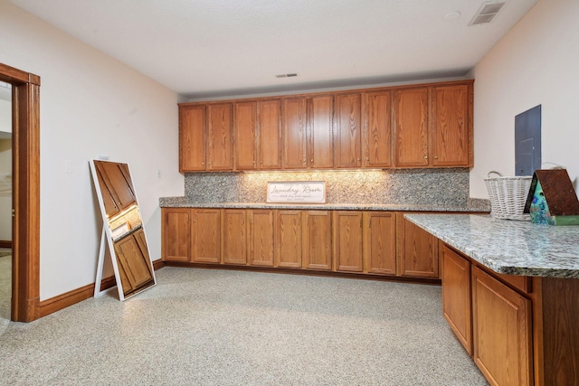 kitchen featuring brown cabinets, visible vents, backsplash, stone countertops, and baseboards