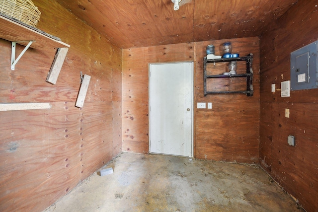 empty room featuring concrete flooring, wooden ceiling, electric panel, and wood walls