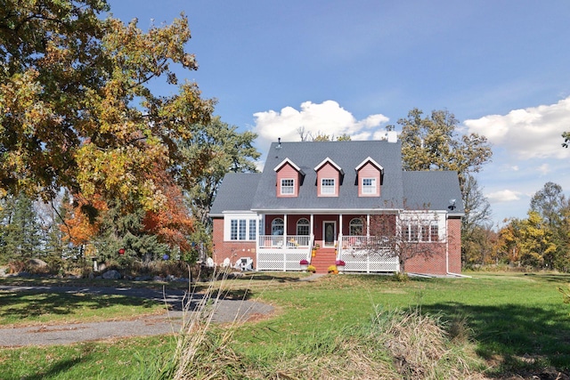 new england style home with covered porch, a front lawn, and brick siding