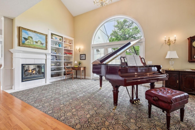 living area featuring baseboards, high vaulted ceiling, a tiled fireplace, and wood finished floors