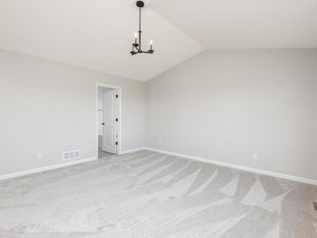 carpeted empty room with lofted ceiling and a chandelier