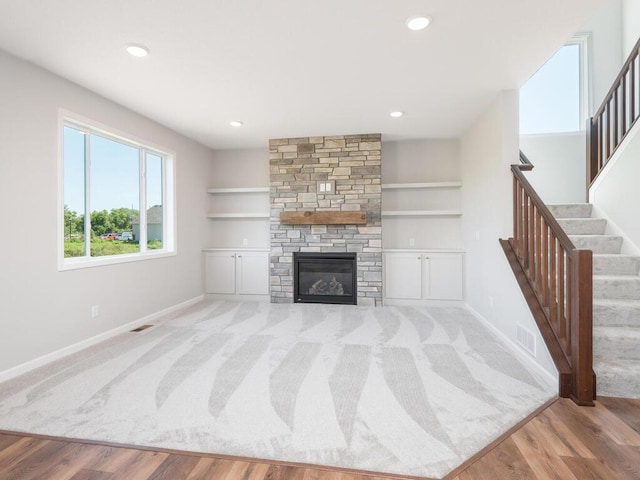 living room with a stone fireplace, built in features, and light wood-type flooring