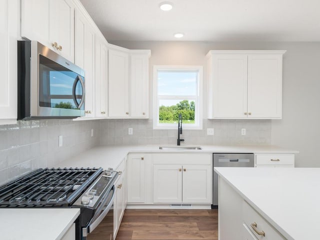 kitchen featuring dark hardwood / wood-style floors, stainless steel appliances, sink, white cabinets, and tasteful backsplash