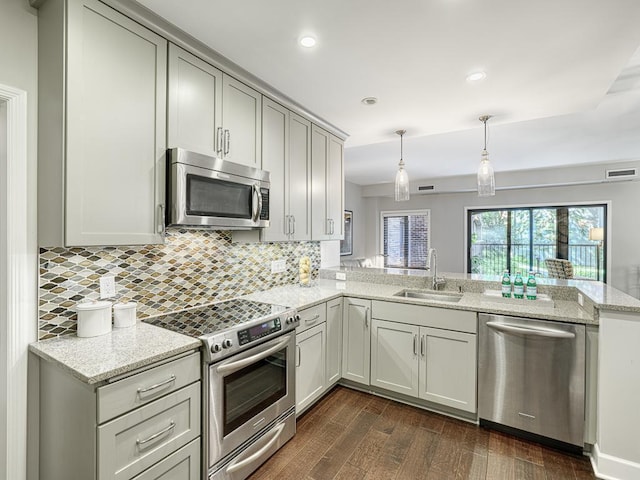 kitchen featuring appliances with stainless steel finishes, decorative light fixtures, sink, light stone counters, and kitchen peninsula