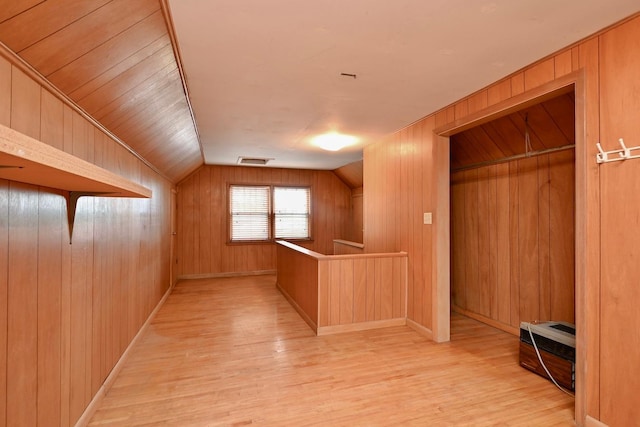 hall with light hardwood / wood-style floors, lofted ceiling, and wood walls