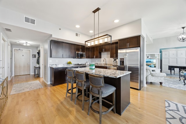 kitchen with a kitchen breakfast bar, decorative light fixtures, light hardwood / wood-style flooring, dark brown cabinets, and stainless steel appliances