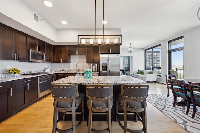 kitchen with light hardwood / wood-style flooring, light stone counters, a breakfast bar area, stainless steel appliances, and pendant lighting