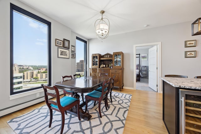 dining space with a dry bar, light wood finished floors, a baseboard radiator, wine cooler, and a chandelier