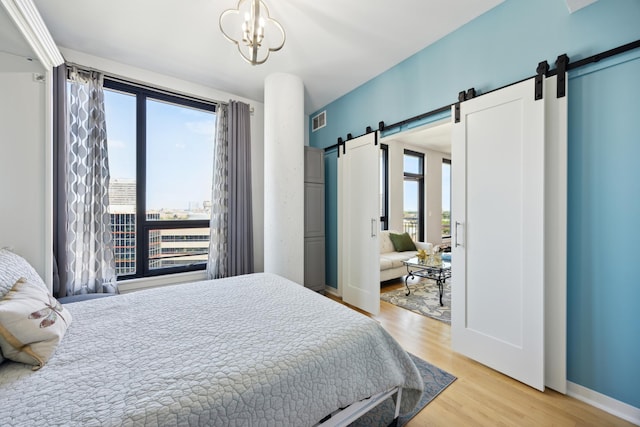 bedroom with a barn door, visible vents, a view of city, light wood-type flooring, and a chandelier