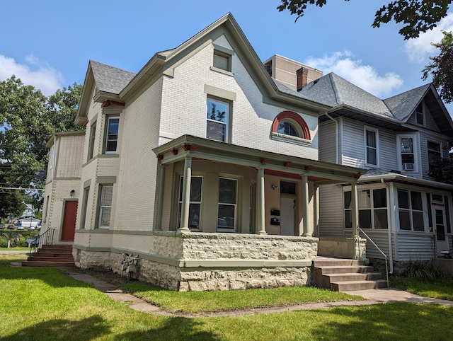 victorian-style house with a front lawn, a porch, brick siding, and roof with shingles