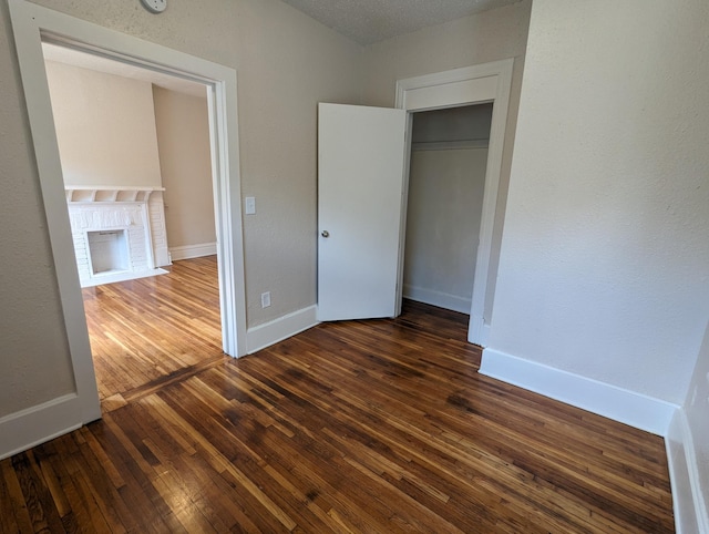 unfurnished bedroom with baseboards, a brick fireplace, and dark wood-style flooring