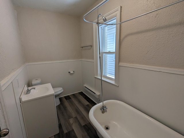 bathroom featuring wood finished floors, a wainscoted wall, a soaking tub, a baseboard heating unit, and toilet