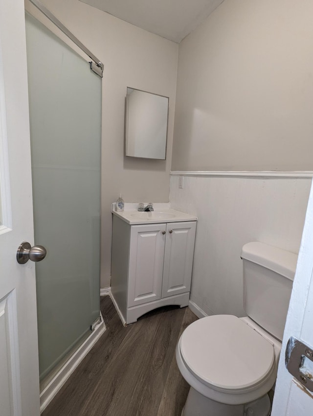 bathroom with a wainscoted wall, toilet, wood finished floors, a shower stall, and vanity