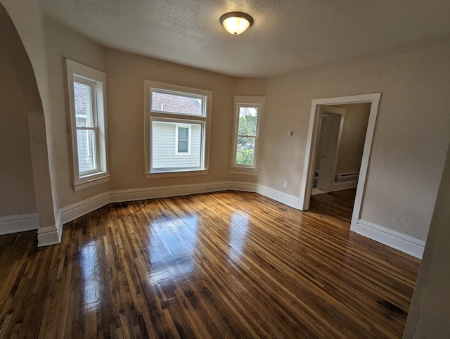 unfurnished room featuring a wealth of natural light, a textured ceiling, baseboards, and dark wood-style flooring