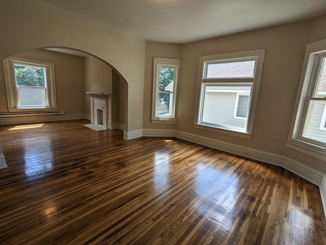 unfurnished living room with dark wood finished floors, a fireplace, and a wealth of natural light