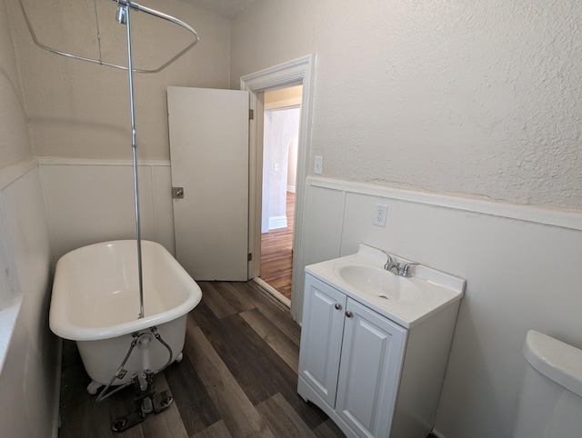 full bath featuring vanity, wood finished floors, a soaking tub, wainscoting, and toilet