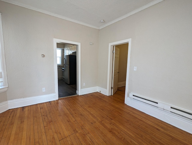 unfurnished room featuring hardwood / wood-style floors, crown molding, baseboards, and baseboard heating