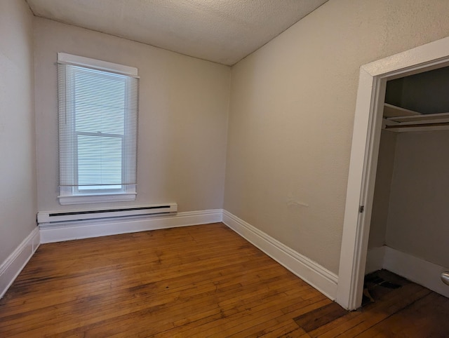 empty room with a baseboard heating unit, baseboards, a textured ceiling, and hardwood / wood-style floors