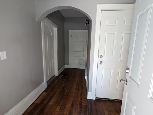 corridor featuring baseboards, arched walkways, and dark wood-style flooring