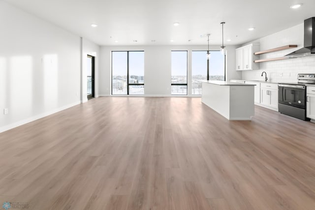 kitchen with wall chimney exhaust hood, stainless steel range with electric cooktop, hanging light fixtures, a kitchen island, and white cabinets