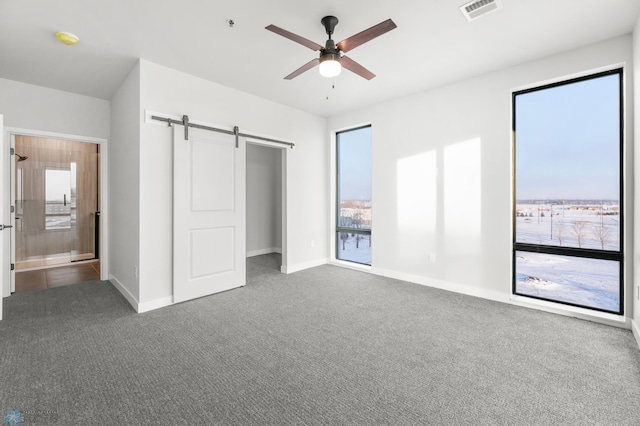 unfurnished bedroom featuring a barn door, ceiling fan, and carpet