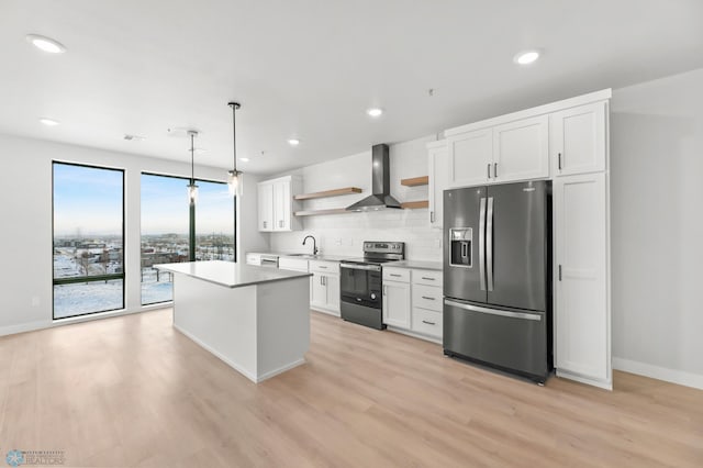 kitchen with wall chimney range hood, hanging light fixtures, stainless steel appliances, white cabinets, and a kitchen island