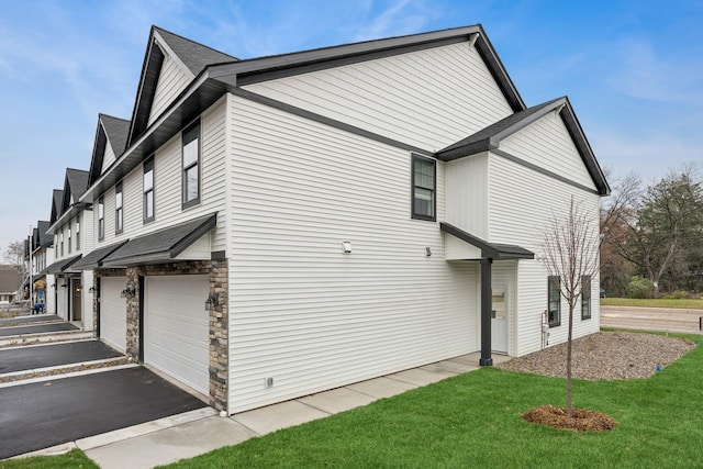 view of side of property with a garage, stone siding, a yard, and driveway