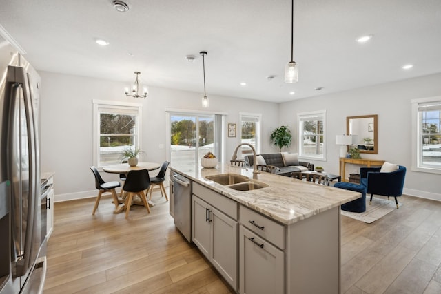 kitchen with appliances with stainless steel finishes, hanging light fixtures, sink, light hardwood / wood-style flooring, and a center island with sink